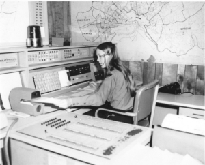 Black and white photo of a dispatcher in front of old computers.