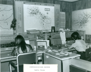 Black and white photo of two dispatchers in front of old computers.