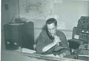 Black and white photo of a man on the phone and using a microphone.